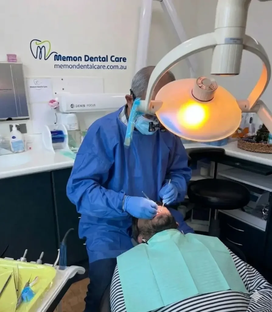 At Memondentalcare clinic, a dentist is treating a patient’s teeth under a bright dental light.